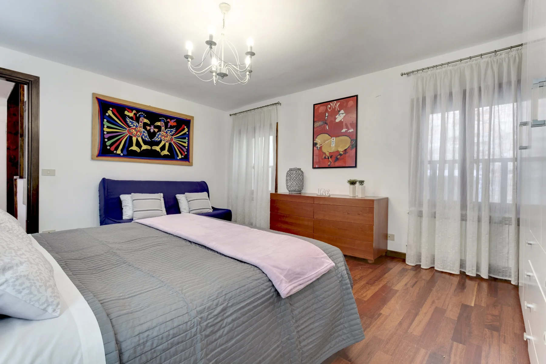 Un dormitorio con una cama, arte colorido en la pared y una cómoda de madera.