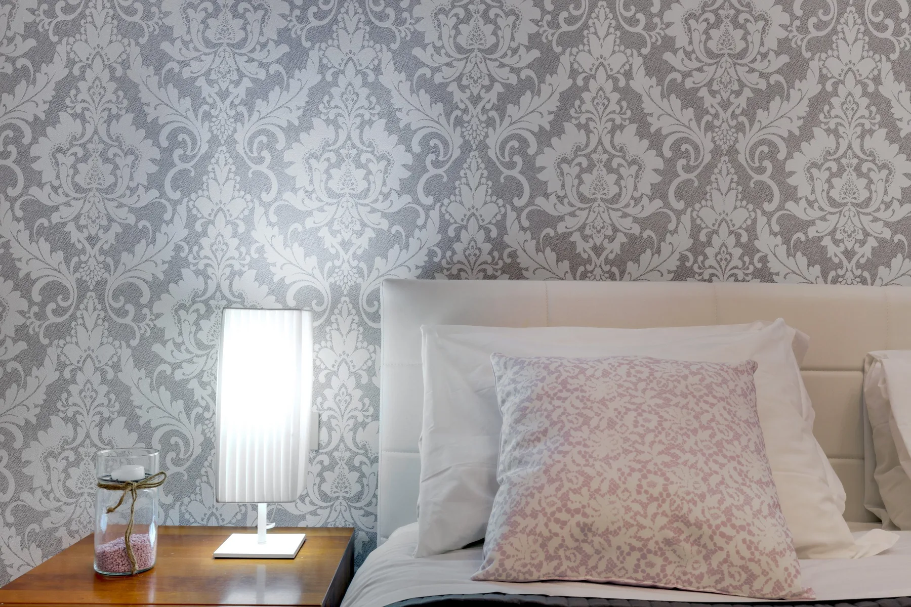 Un dormitorio con papel pintado estampado y una cama junto a una lámpara encendida.