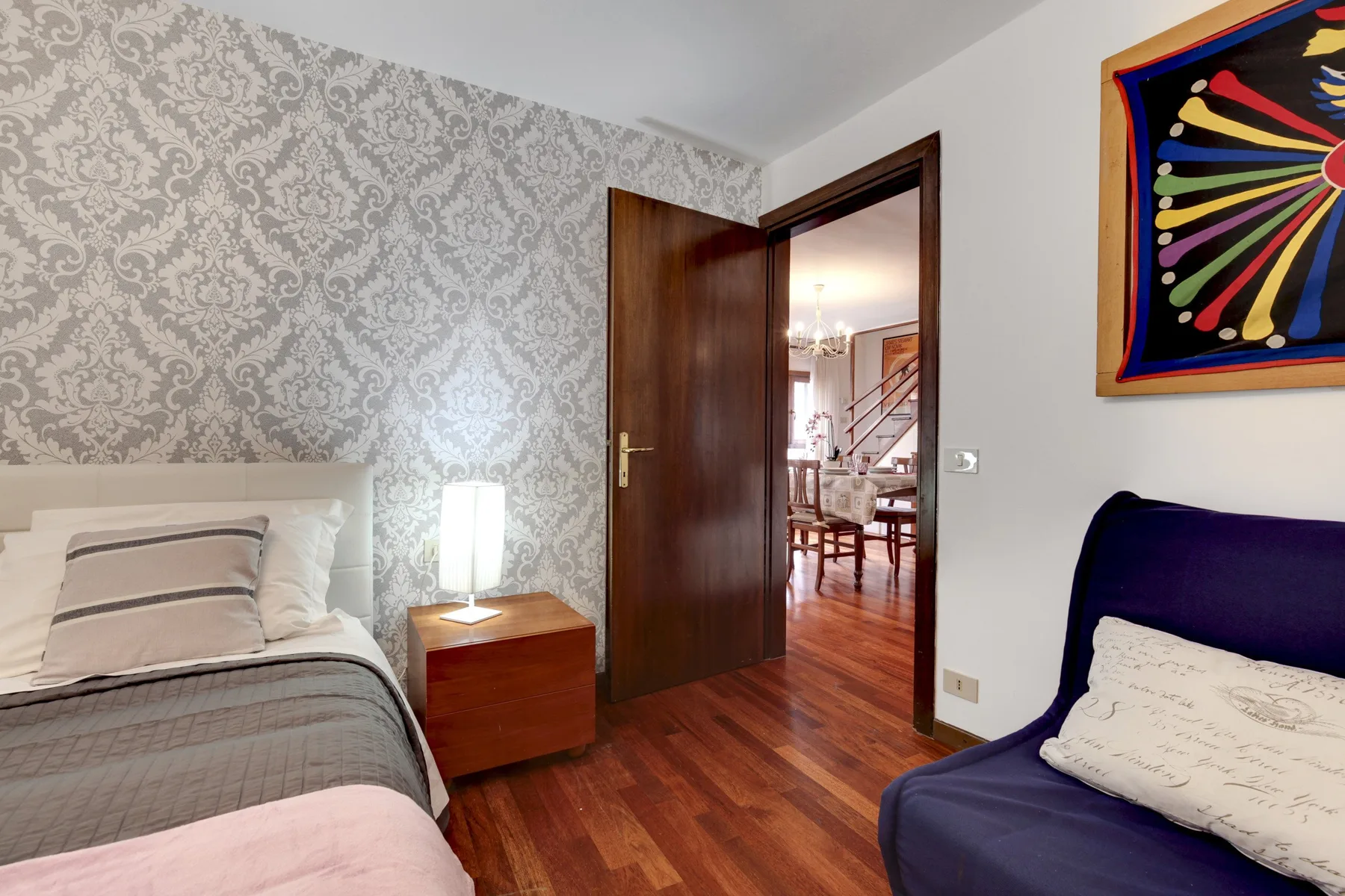Un dormitorio con una cama, una mesita de noche y una puerta abierta hacia un comedor.