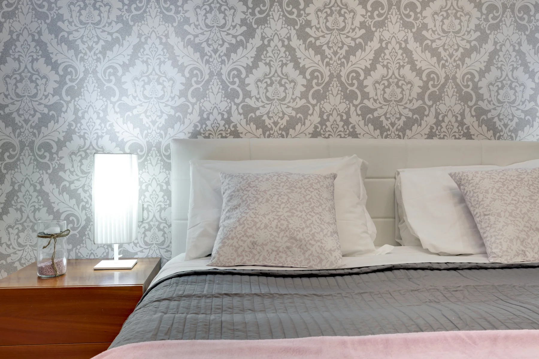 Un dormitorio con una cama vestida con ropa de cama gris y papel tapiz estampado.