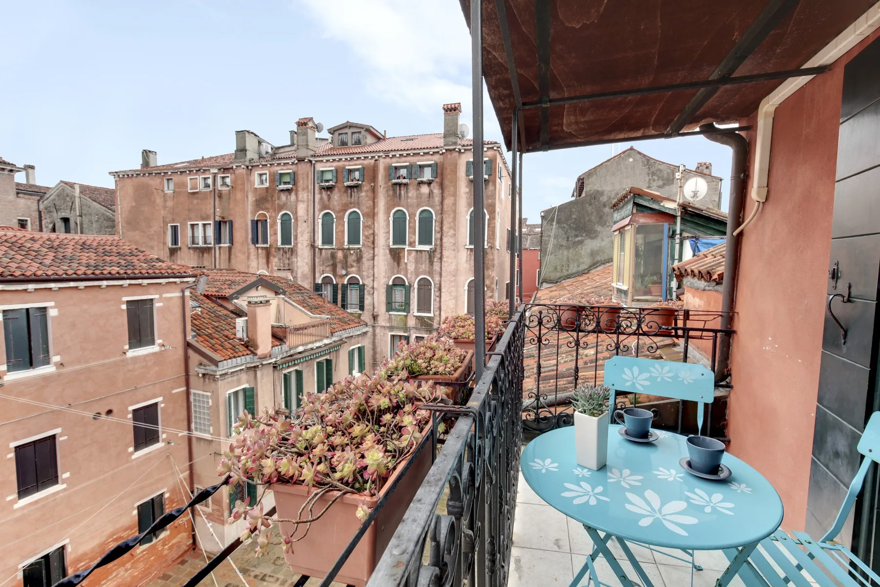 Una terraza en la azotea con una mesa turquesa y vistas a los edificios cercanos.