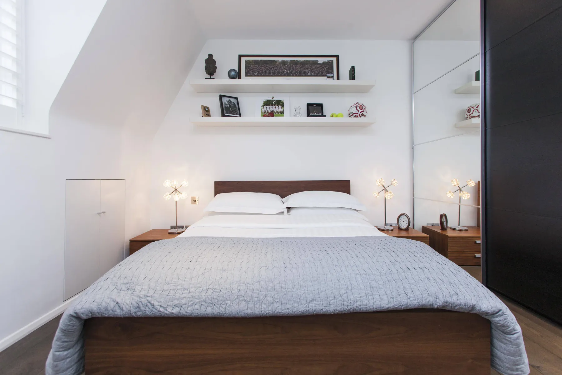 Un dormitorio luminoso con una cama doble bajo estantes en la pared.