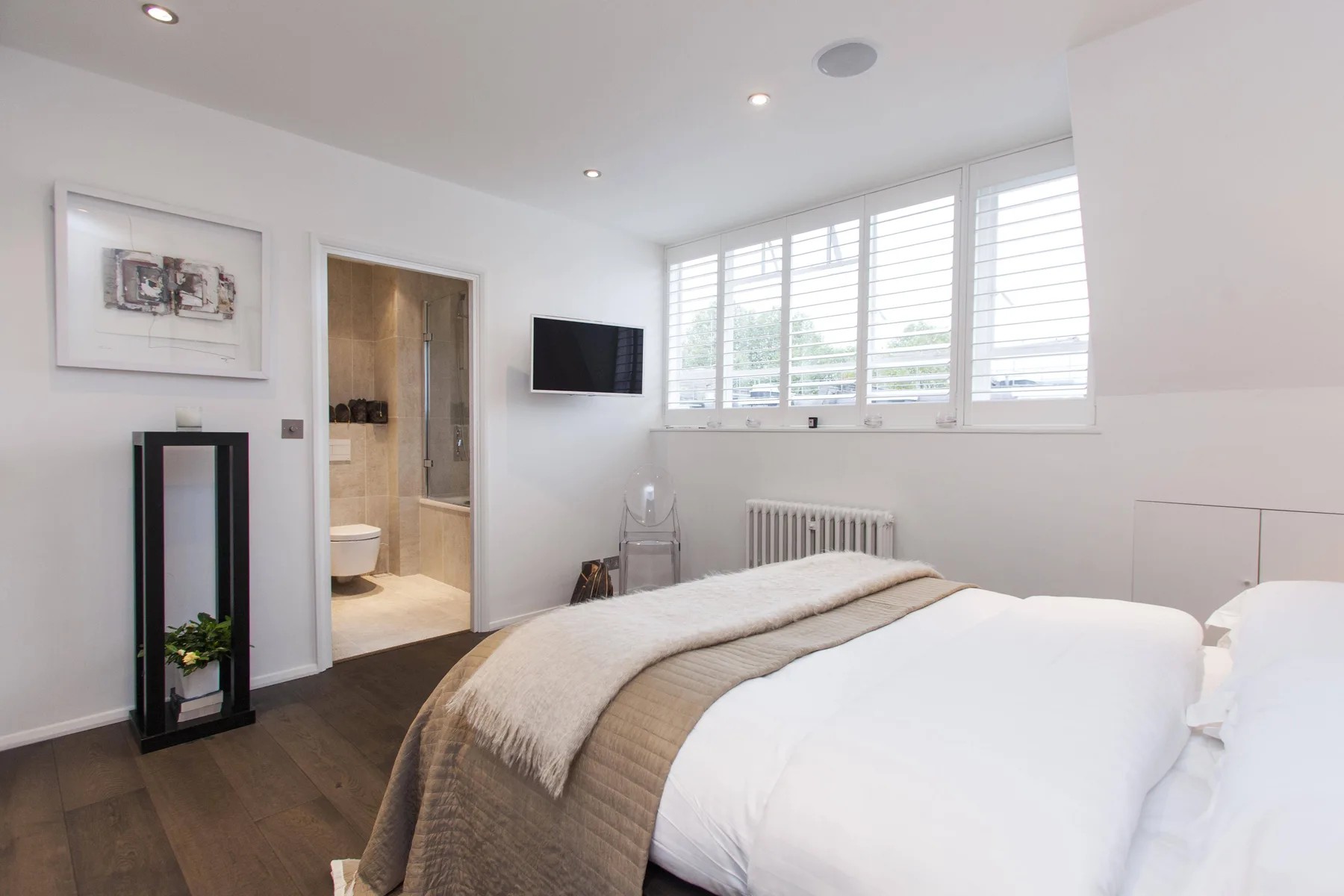 Un dormitorio luminoso con una cama bien hecha bajo amplias ventanas.