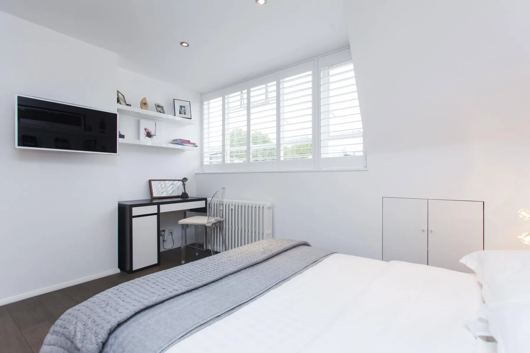Un dormitorio luminoso con cama, escritorio y ventanas amplias.