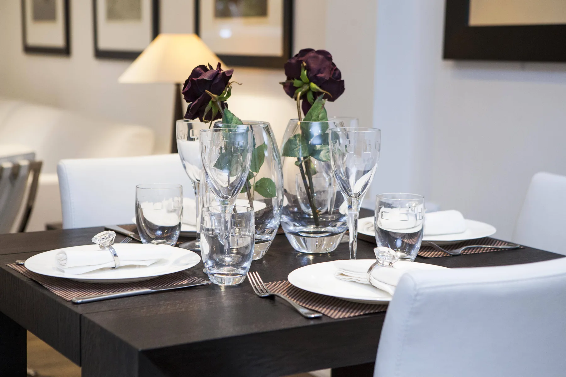 A dining table is set with plates, glassware, and dark flowers.