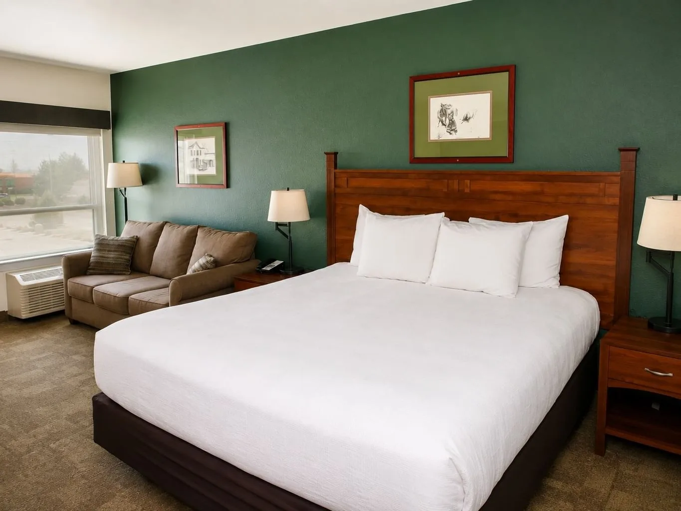 King room with white bedding, wooden headboard, green accent wall, and seating area