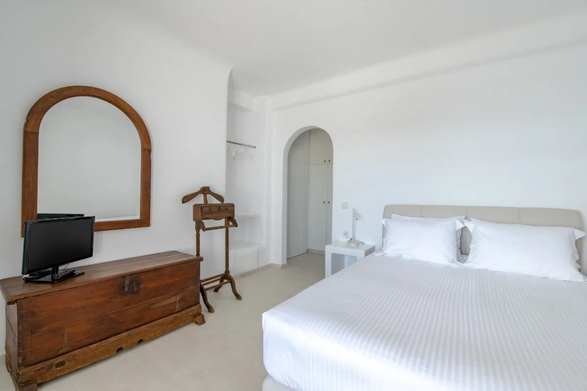 A bright bedroom with a neatly made bed, wooden dresser, and arched mirror.