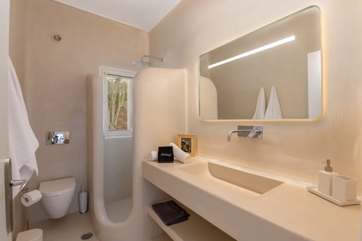 A bathroom with a walk-in shower, wall-mounted toilet, and illuminated mirror.