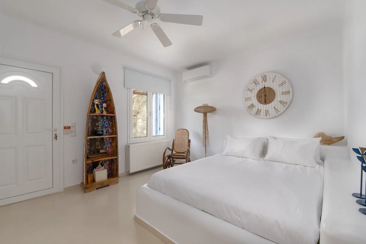 A bright bedroom with a white bed, a window, and a large wall clock.