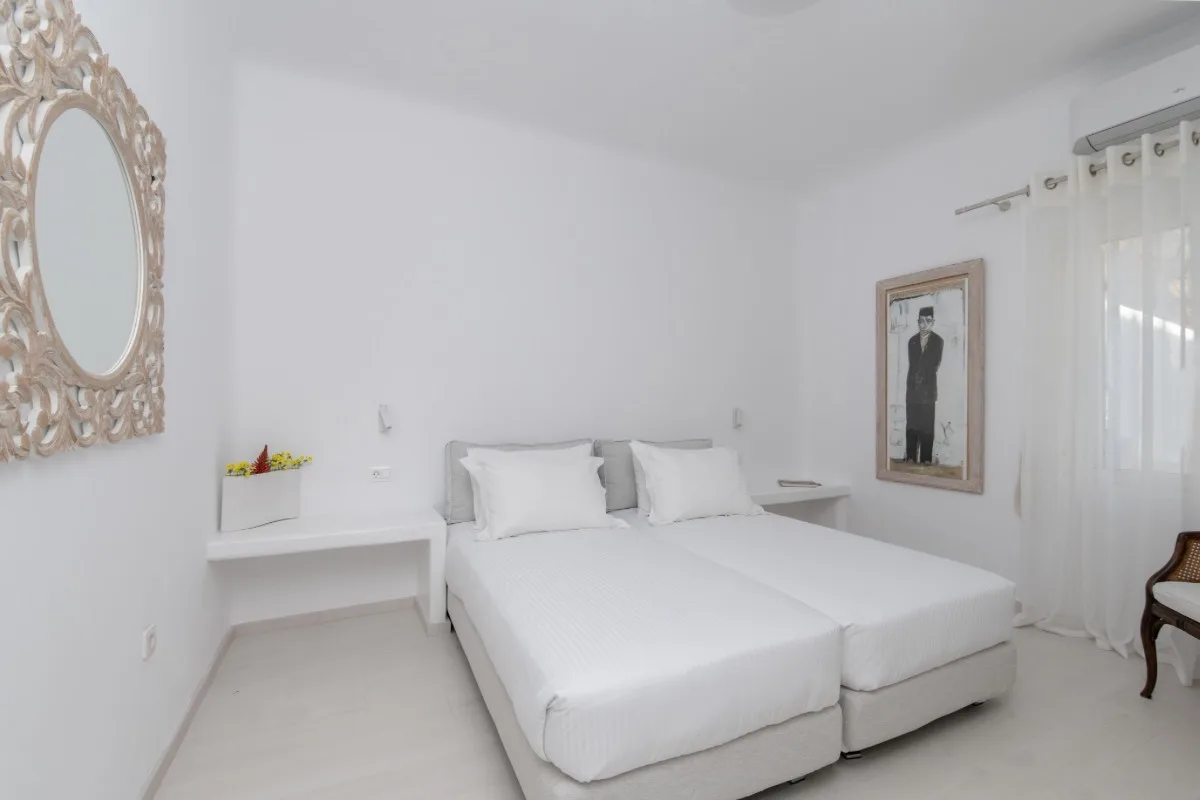 A bright bedroom with white bedding, bedside shelves, and a framed portrait.