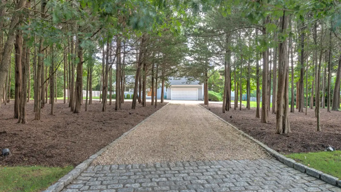 Un camino de grava atraviesa una zona arbolada y llega hasta un garaje.