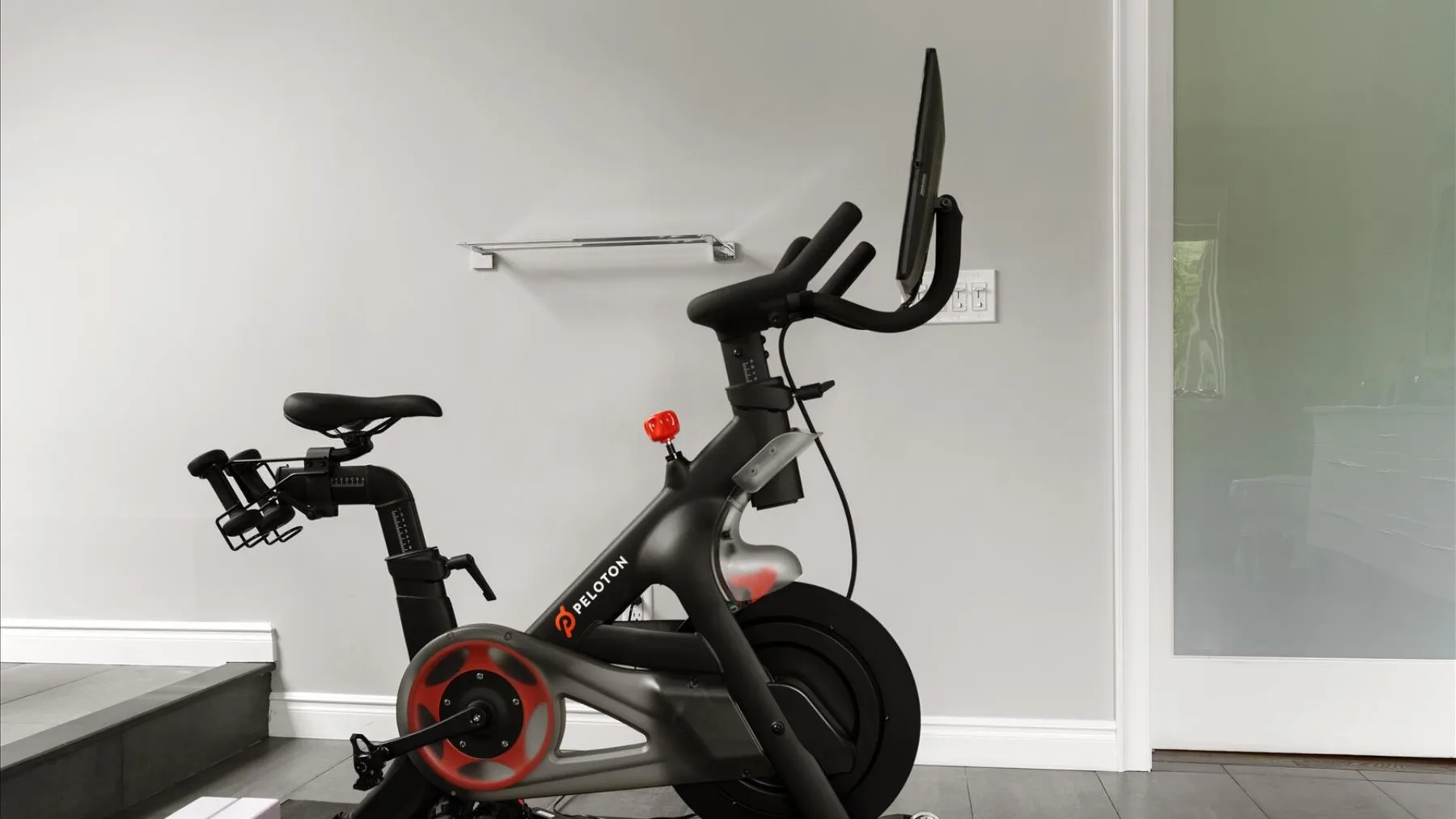 Una bicicleta estática está en una habitación luminosa junto a una puerta de vidrio.