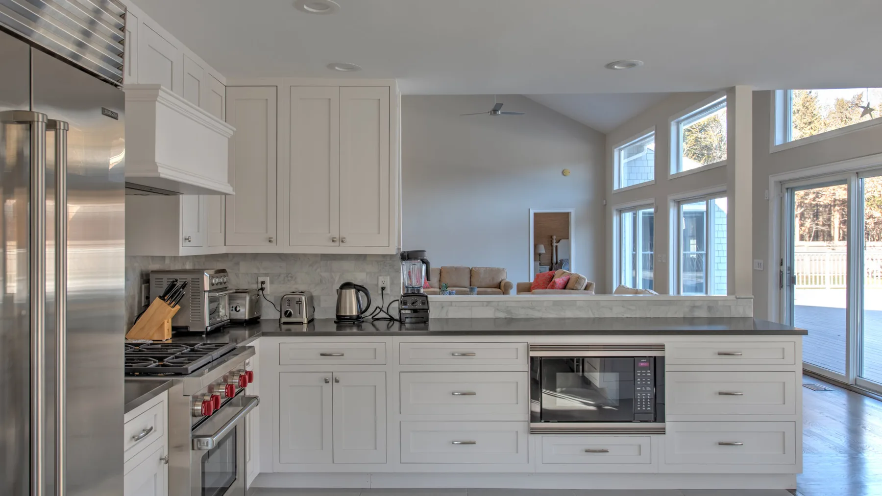 Una cocina luminosa con gabinetes blancos, electrodomésticos de acero inoxidable y ventanas grandes.