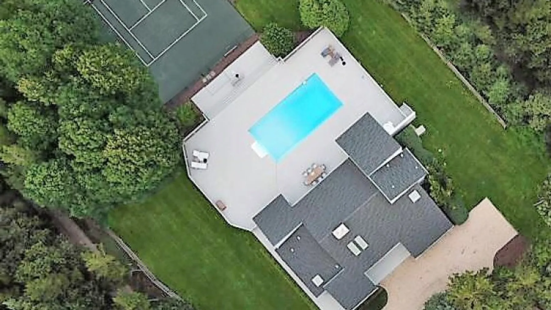 Una vista aérea muestra una casa junto a una piscina y una cancha de tenis.