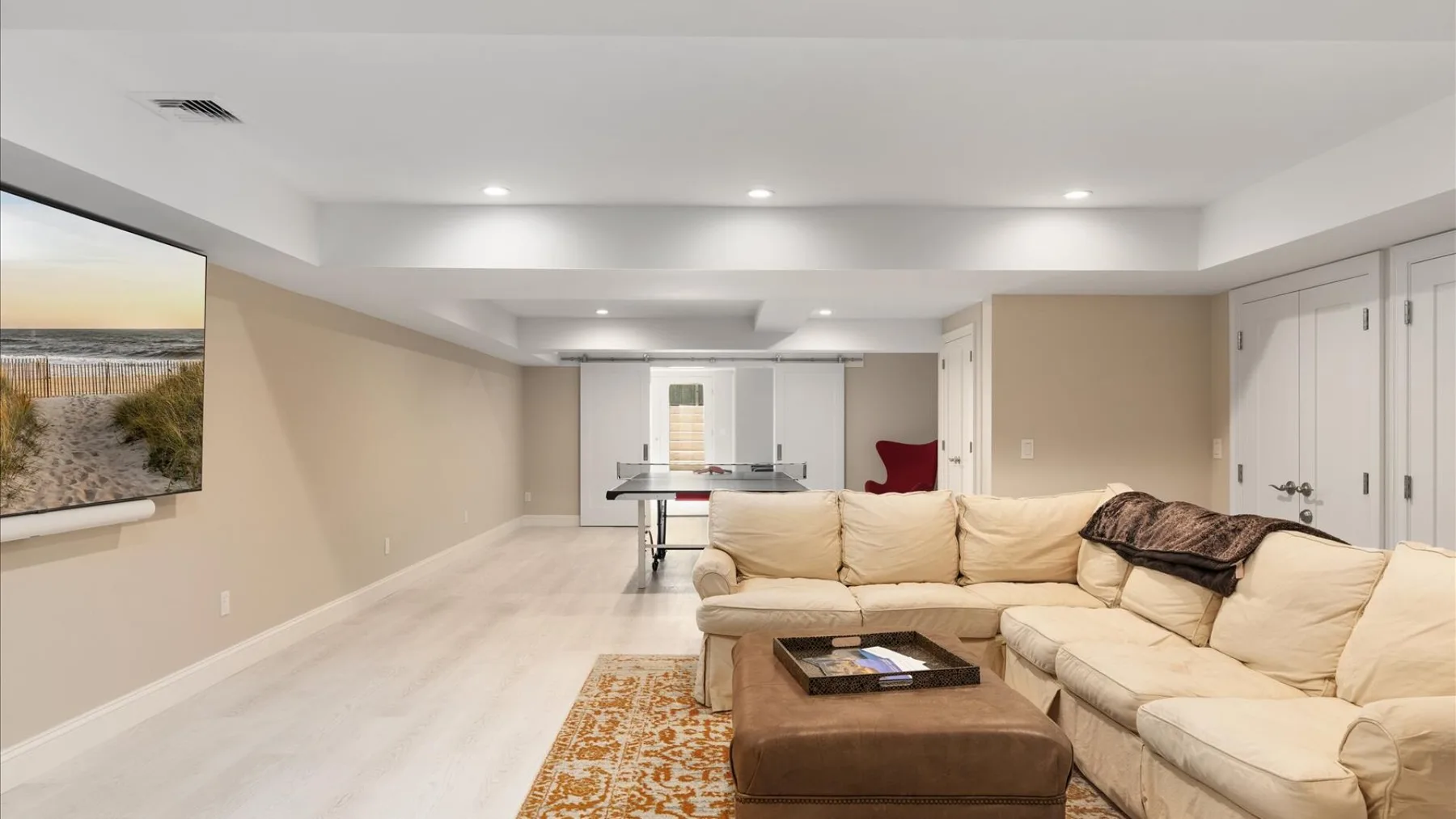 Una sala de estar con asientos color crema y una mesa de centro frente a un televisor.