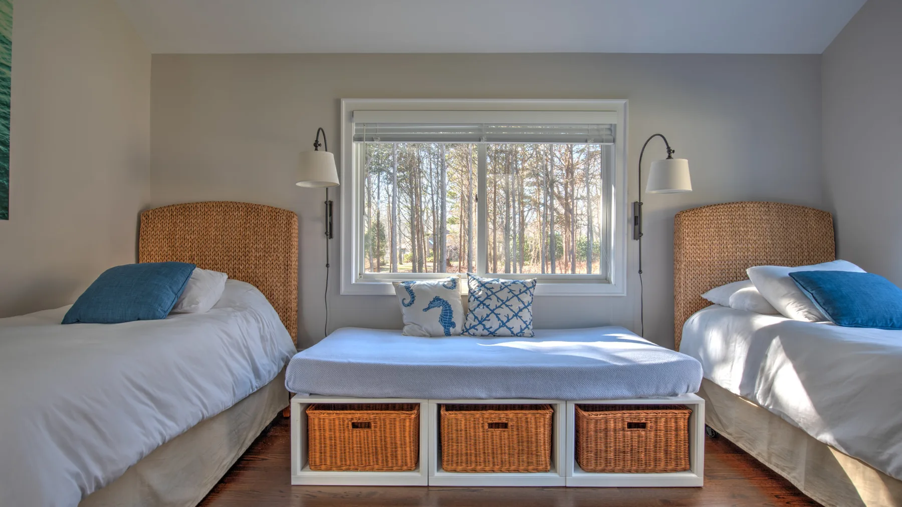 Un dormitorio luminoso con dos camas, una ventana y un banco bajo entre ellas.