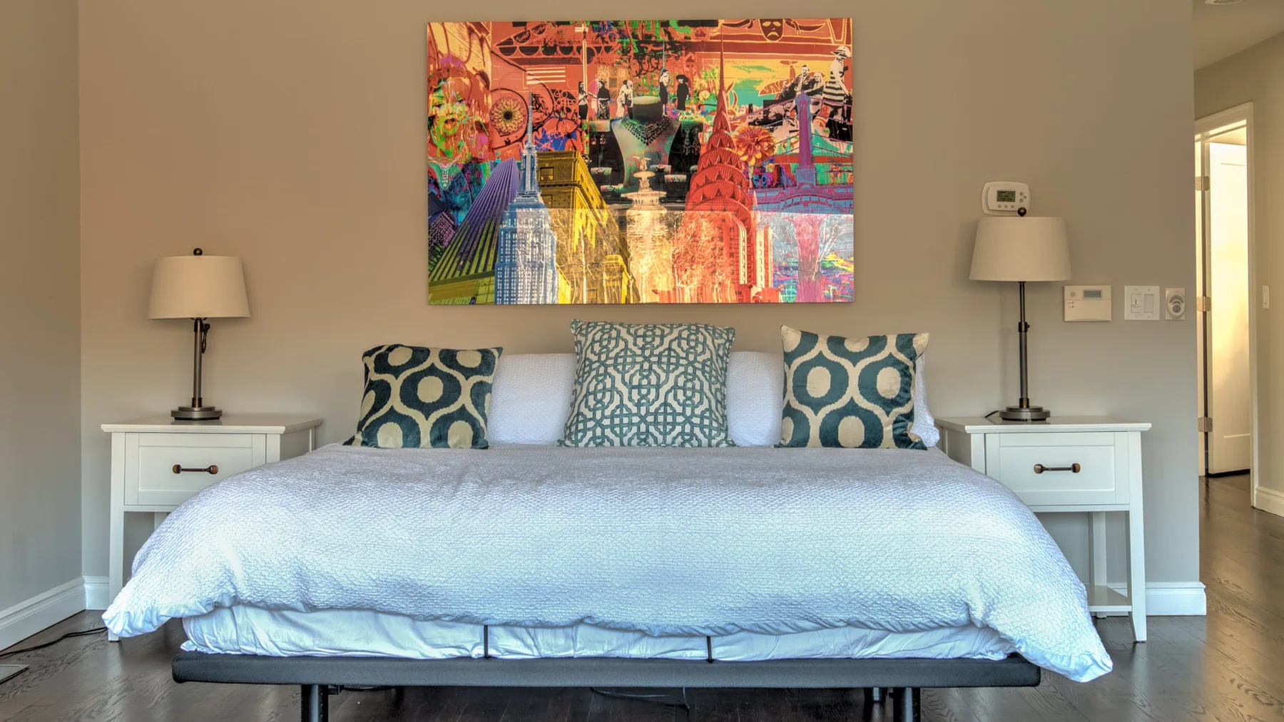Un dormitorio con una cama tendida, mesitas de noche a juego y arte colorido en la pared.