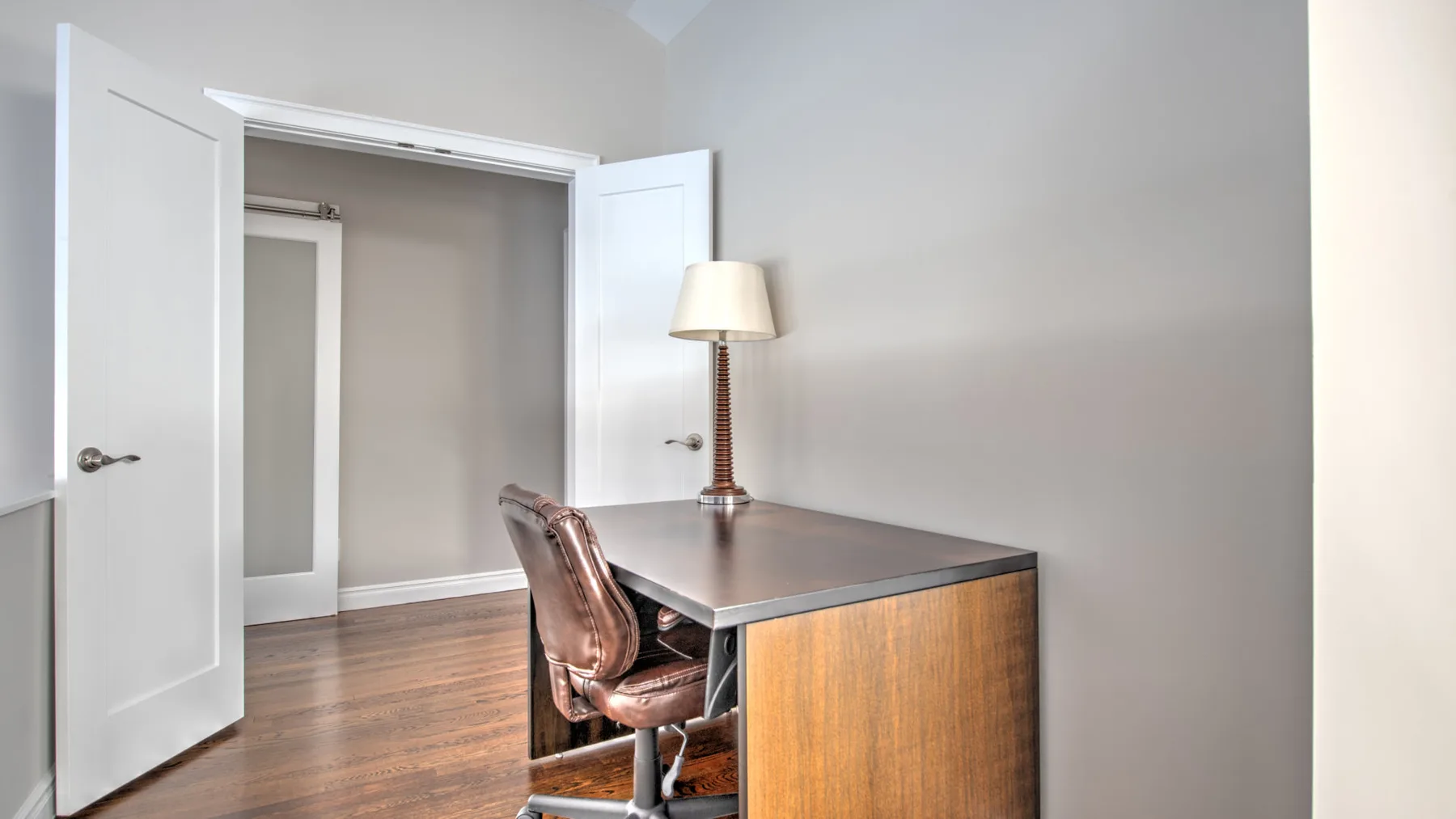 Un escritorio pequeño está en una habitación luminosa con puertas abiertas y piso de madera.