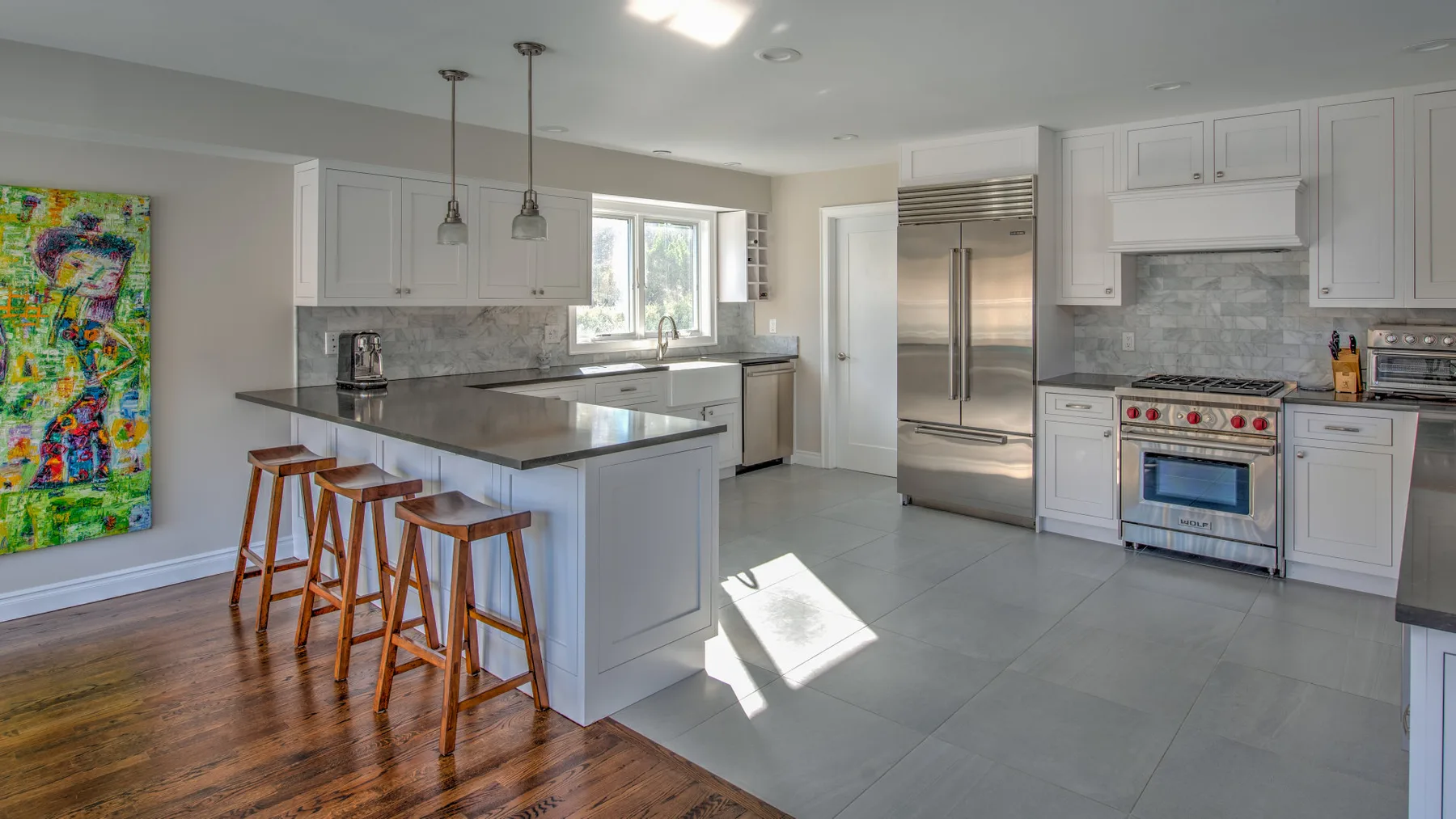 Una cocina luminosa con una isla central, electrodomésticos de acero inoxidable y piso gris.