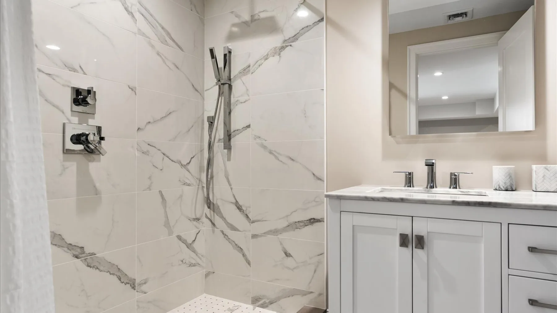Un baño luminoso con ducha de cristal y un tocador blanco.