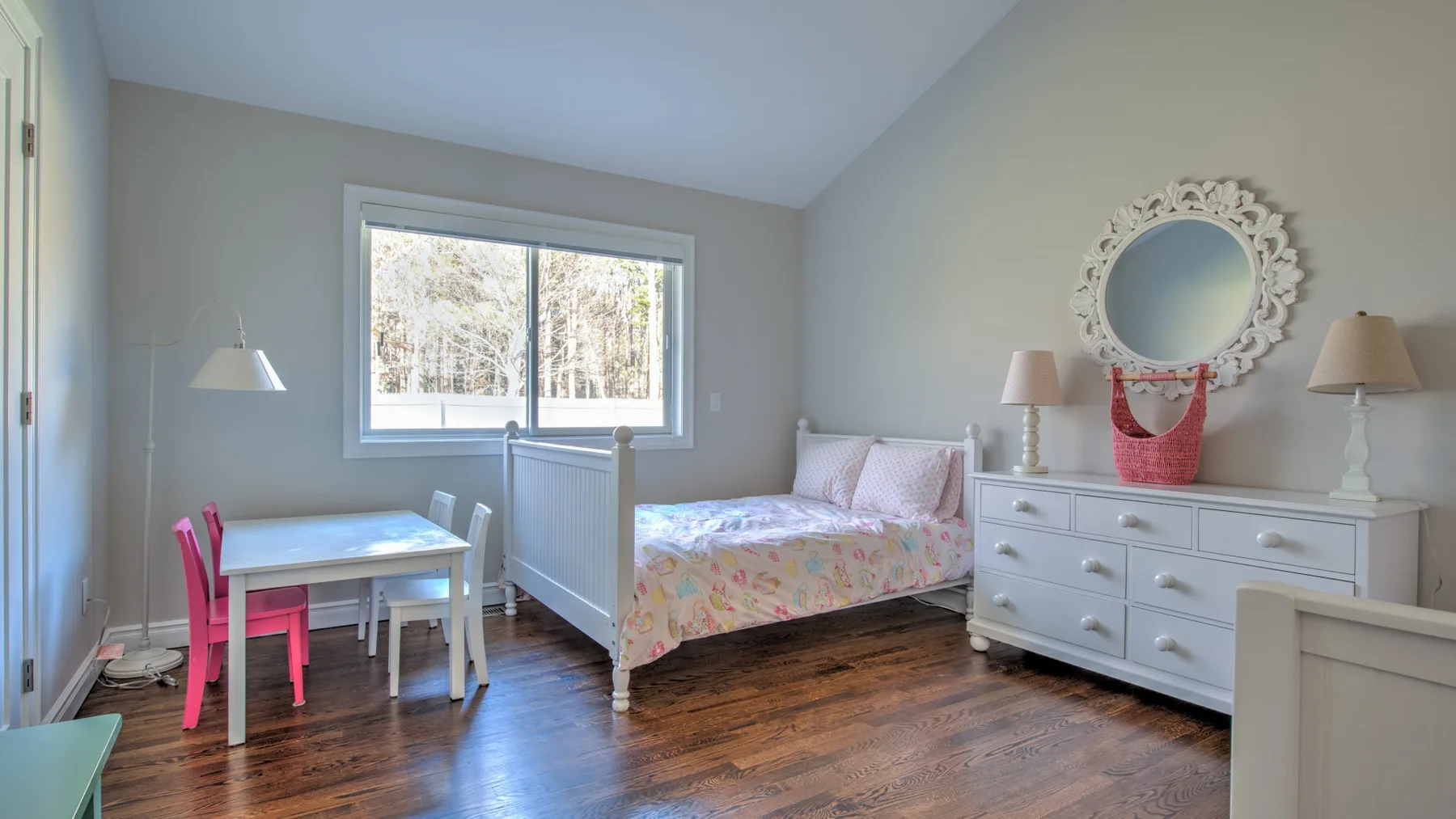 Un dormitorio luminoso con una cama, un escritorio y una ventana grande.