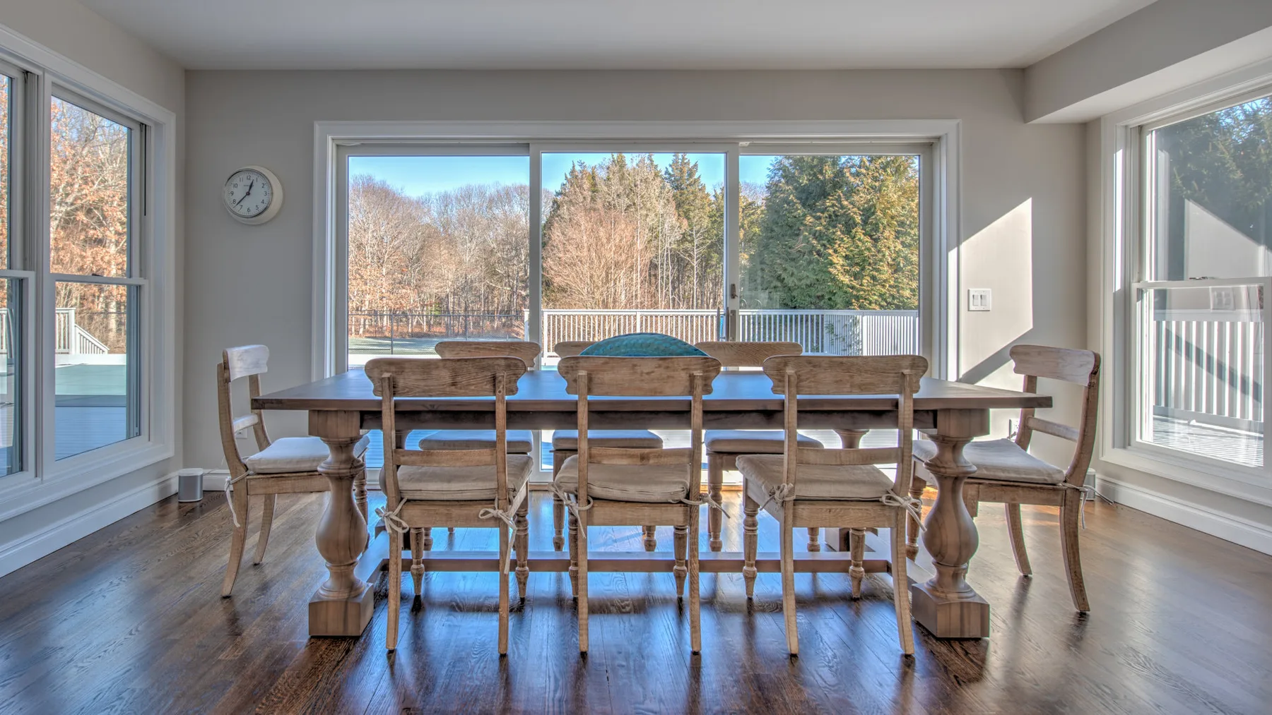 Un comedor con una mesa de madera y asientos junto a grandes ventanas.