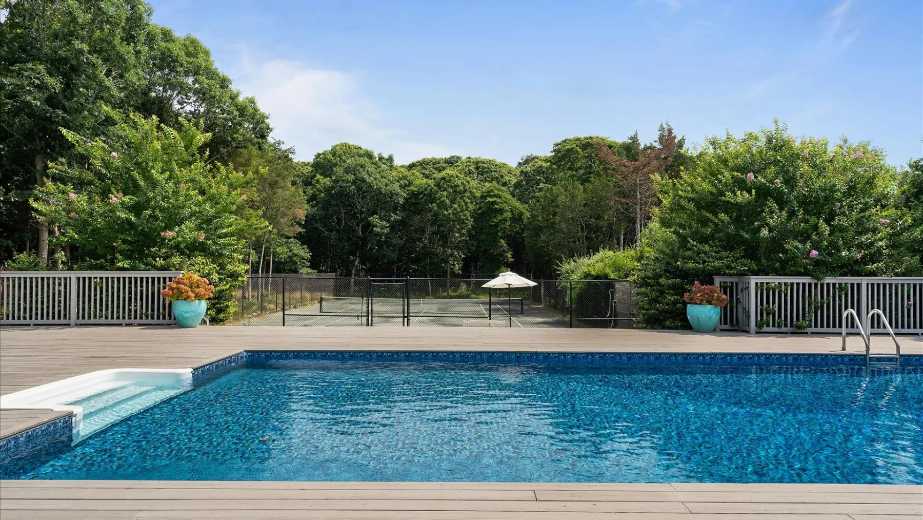 Una piscina al aire libre está junto a una terraza de madera y árboles frondosos.