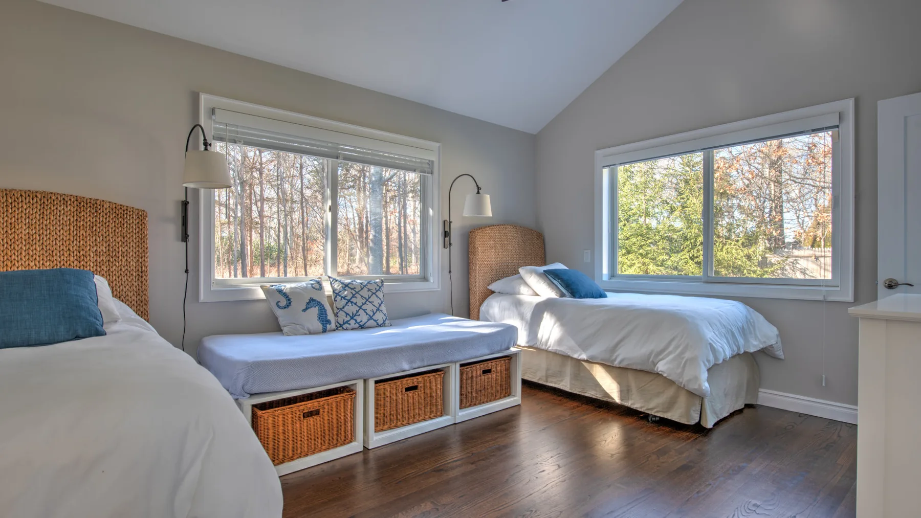 Un dormitorio luminoso con varias camas y grandes ventanas con vistas a los árboles.