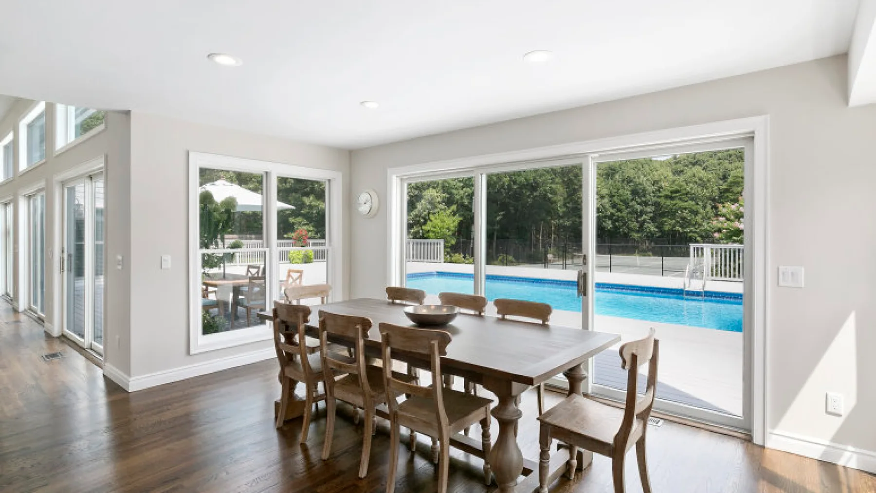 Comedor con una mesa larga de madera junto a grandes ventanas con vista a una piscina.