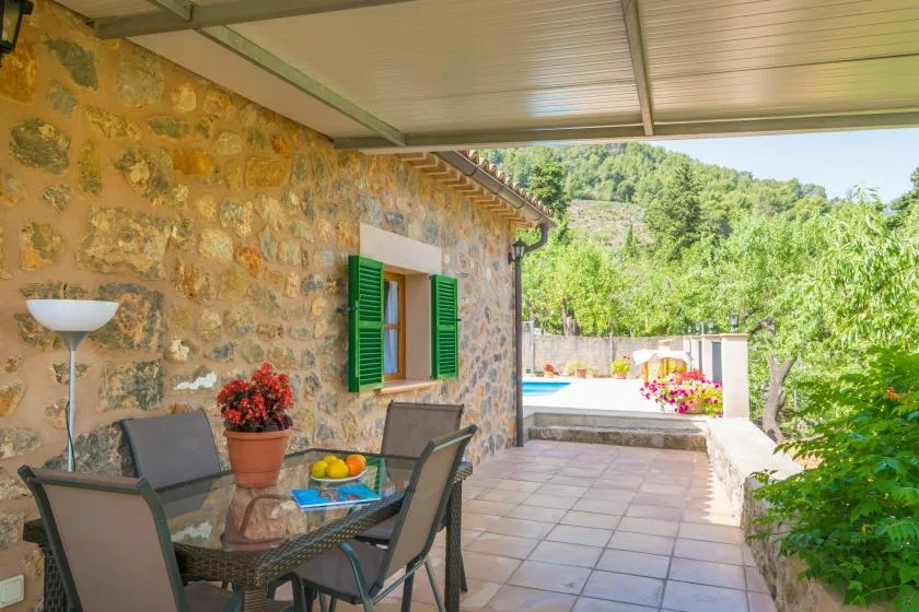 A stone-walled patio with outdoor seating and green shutters overlooks a garden.