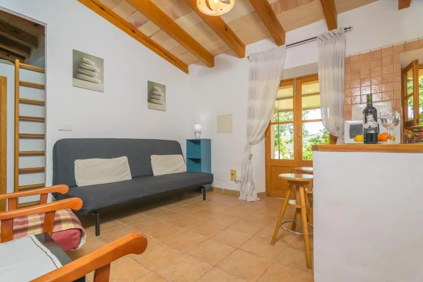 A bright living area with a dark sofa, wooden ceiling beams, and a dining counter.