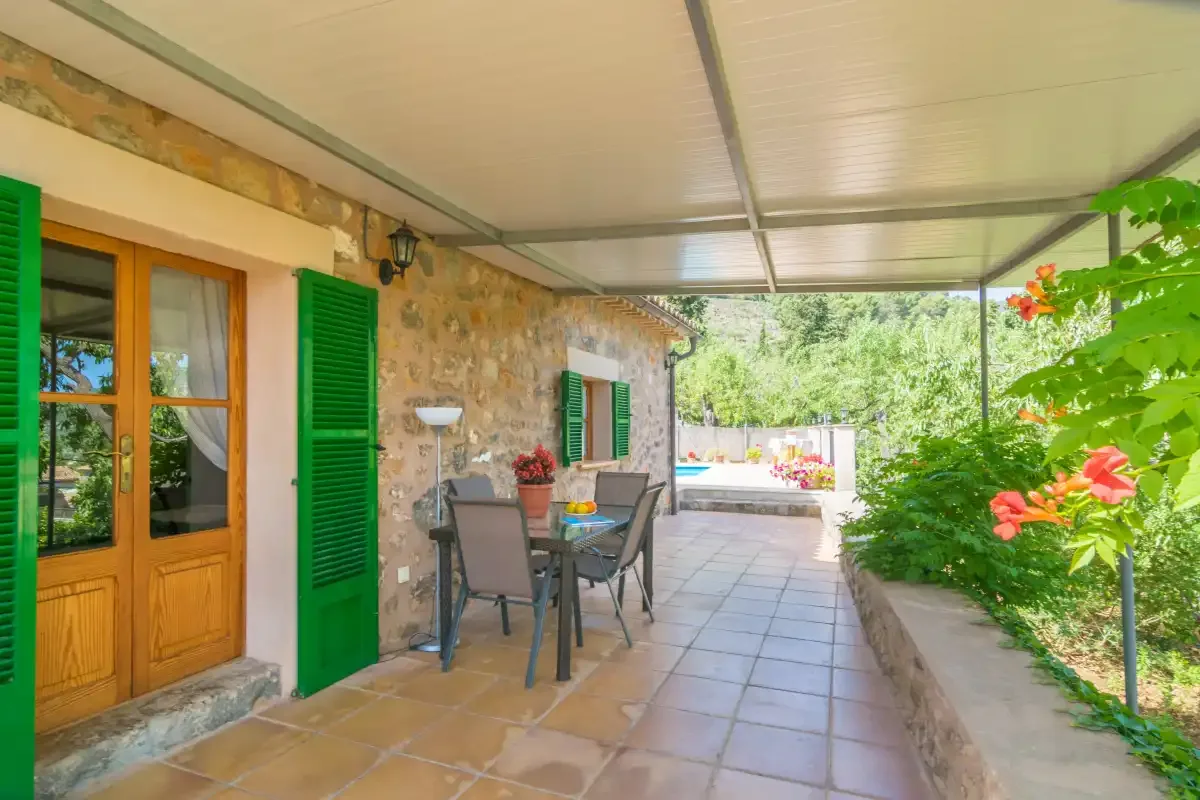 A covered stone patio with outdoor seating and a garden beside it.
