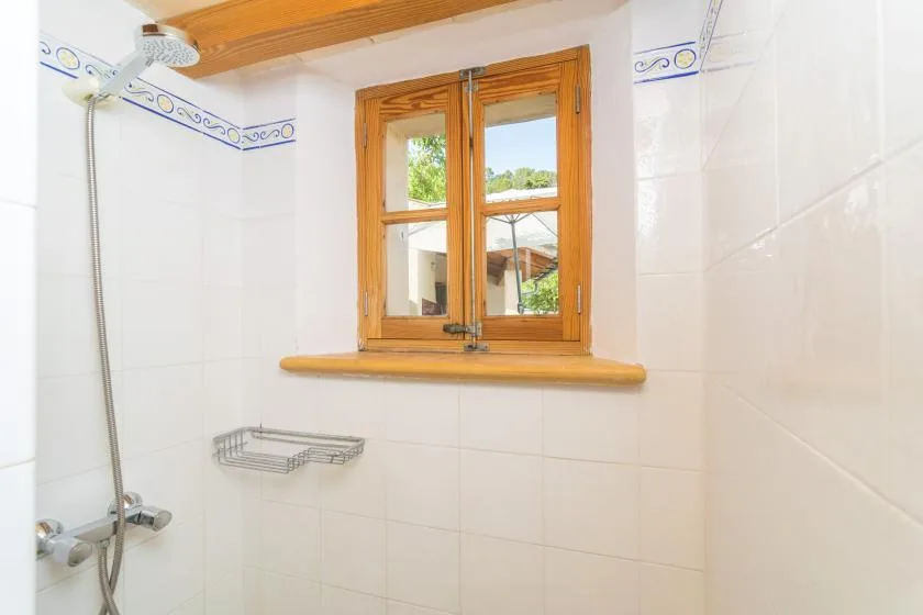 A tiled bathroom with a shower and a wooden-framed window.
