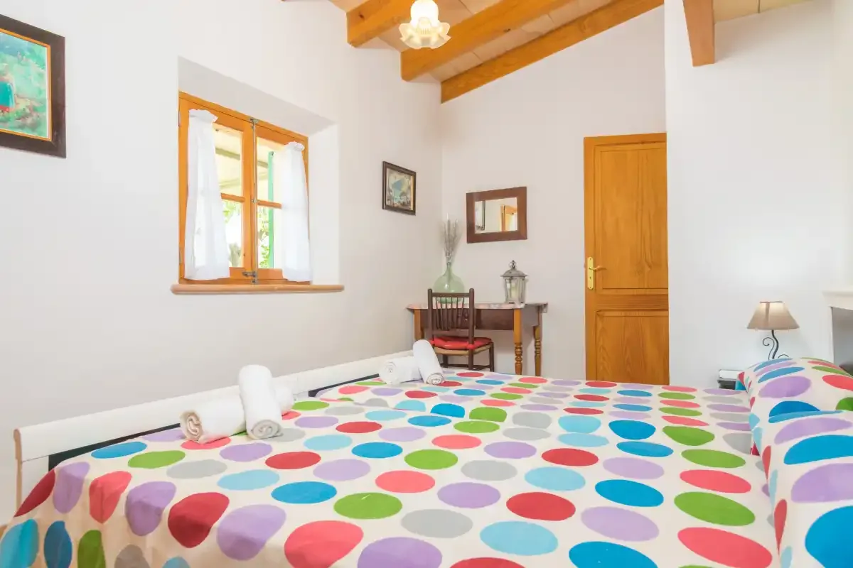 A bedroom with a colorful polka-dot bedspread, wooden beams, and a window.