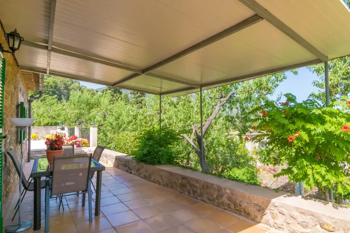 A covered outdoor patio with a dining table and surrounding greenery.