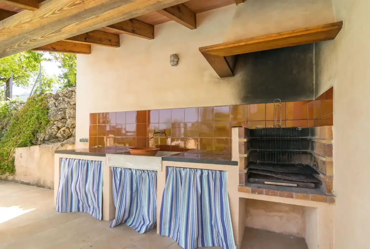 A covered outdoor cooking area with a tiled counter and built-in grill.
