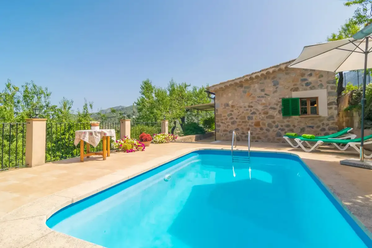 An outdoor swimming pool beside a stone building, with sun loungers and an umbrella.