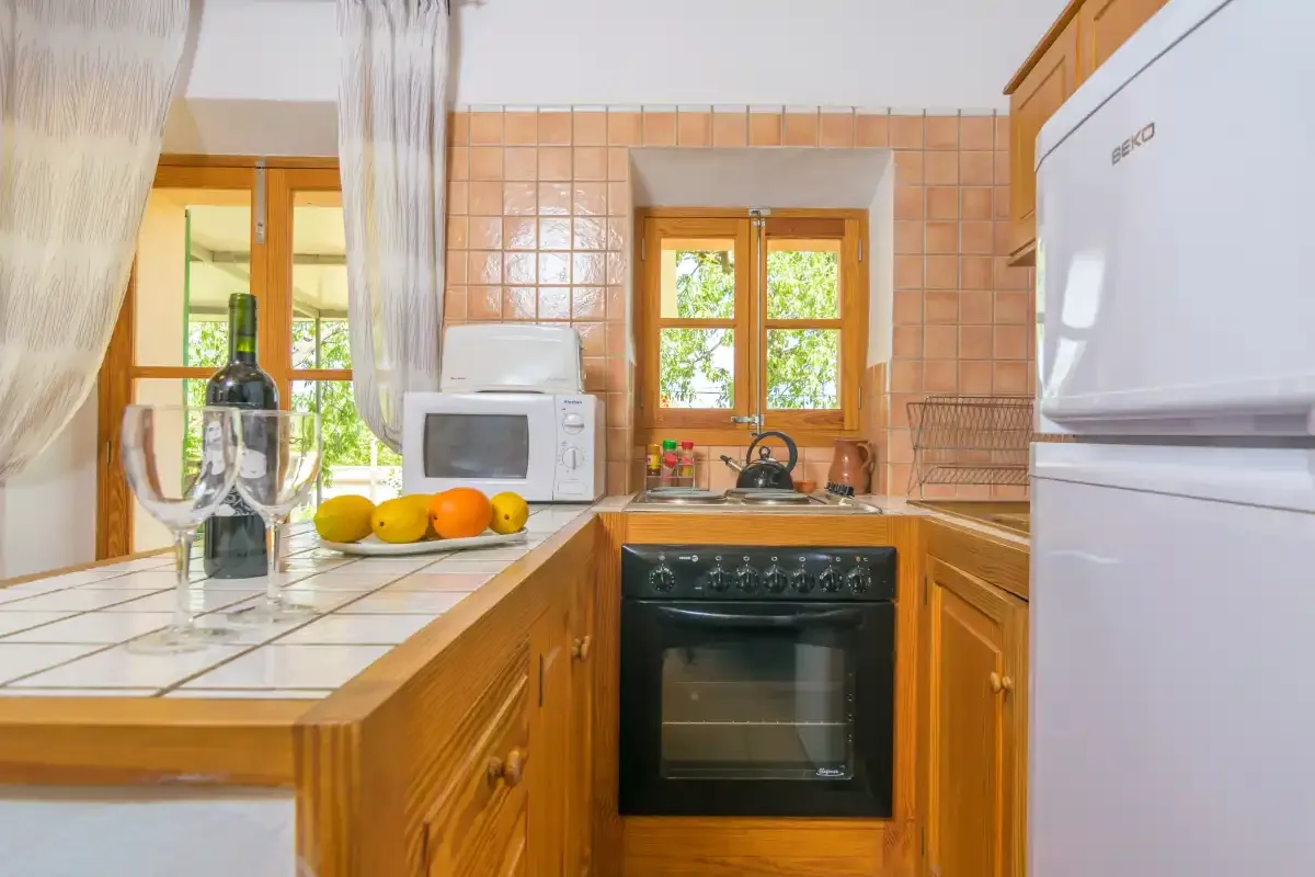 A kitchen with wooden cabinets, tiled counters, and a window above the stove.