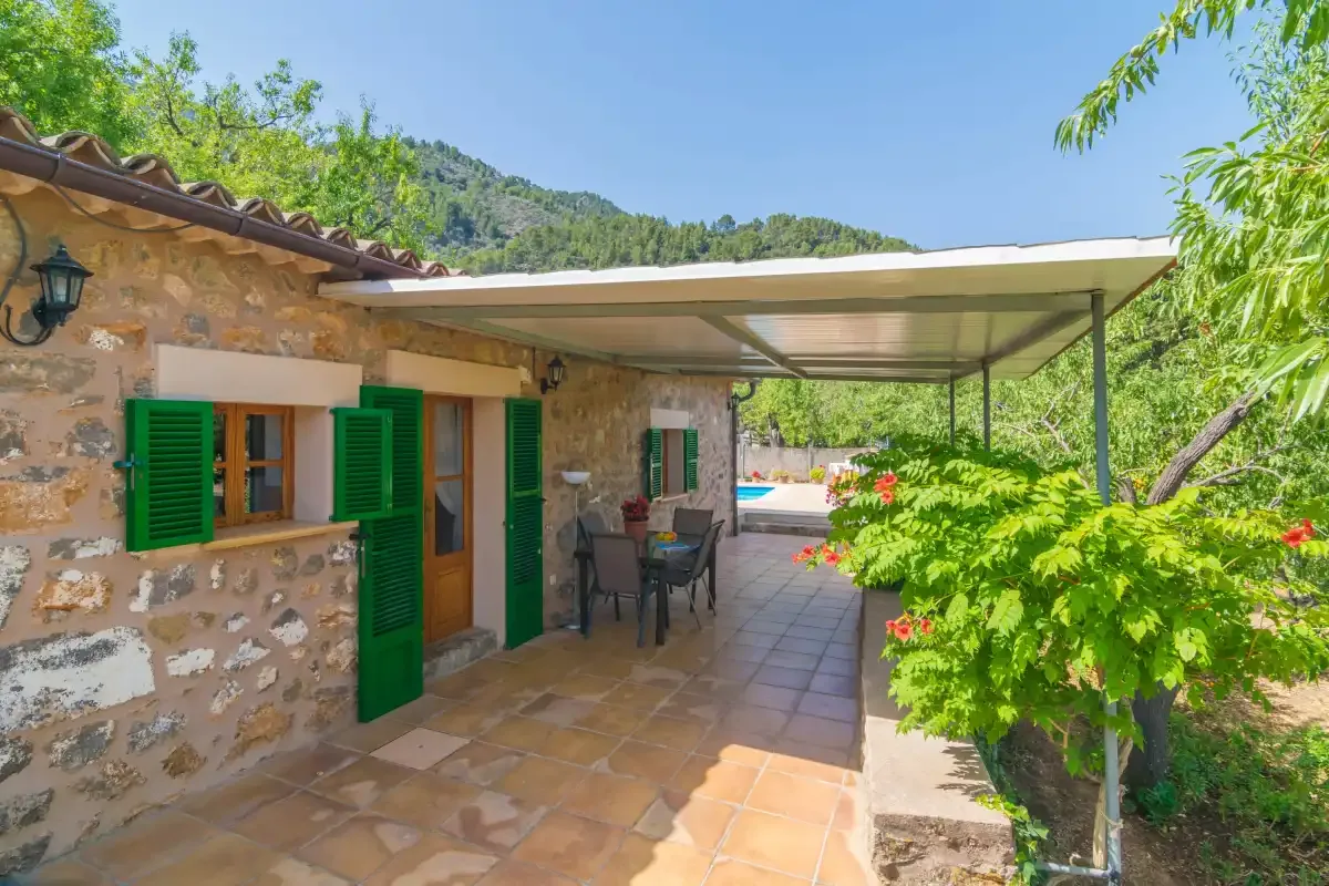 A stone patio with green shutters, outdoor seating, and a leafy garden.