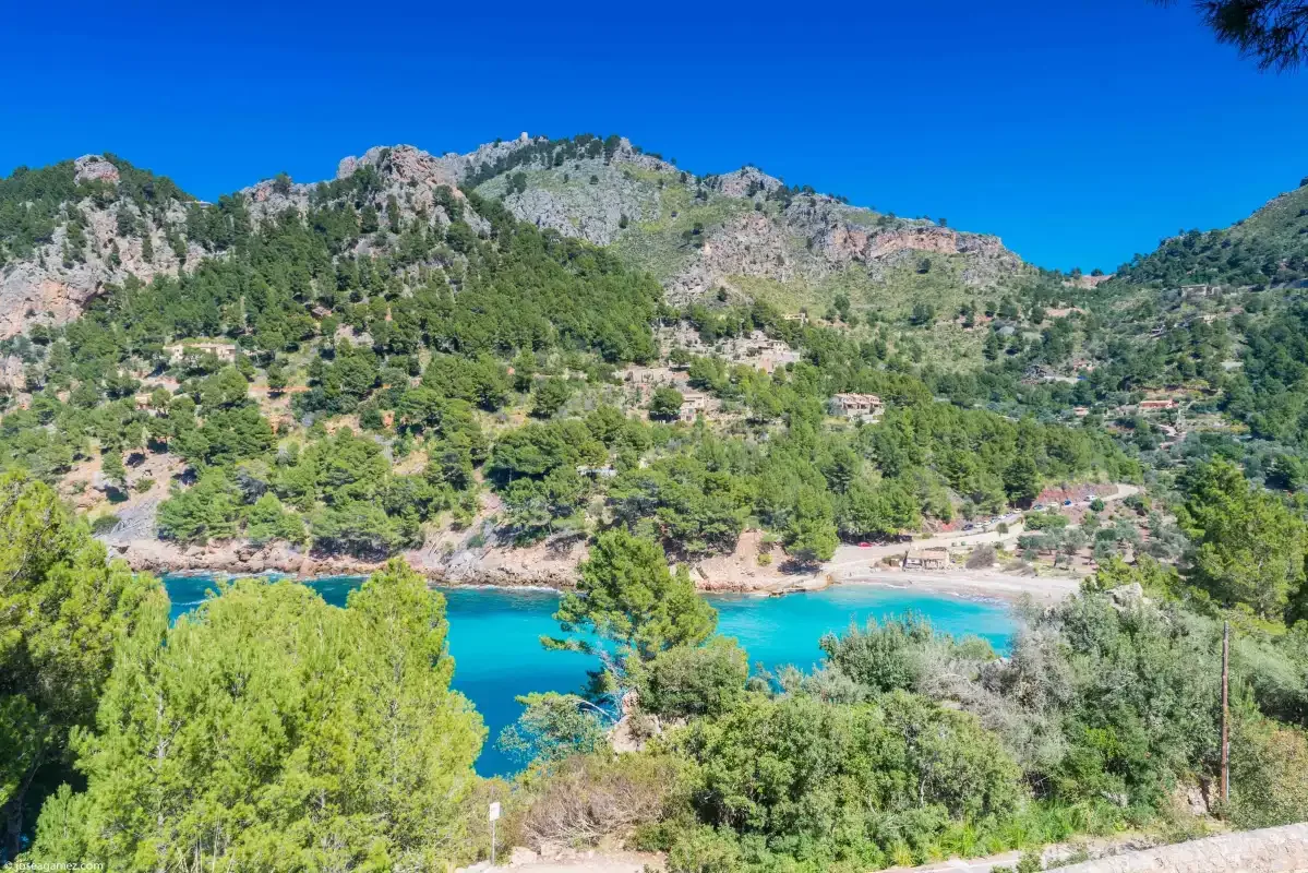 A turquoise lake sits below a green, rocky mountain slope.