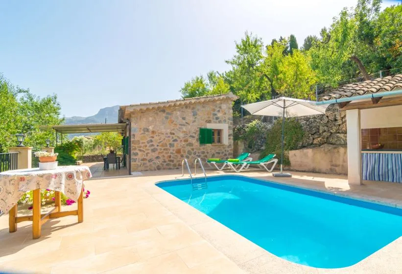 An outdoor swimming pool sits beside a stone building and a shaded seating area.
