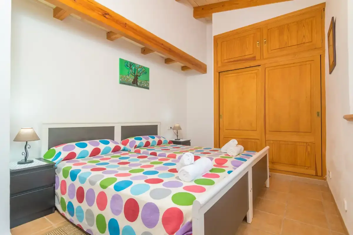 A bedroom with colorful patterned bedding and a wooden wardrobe.
