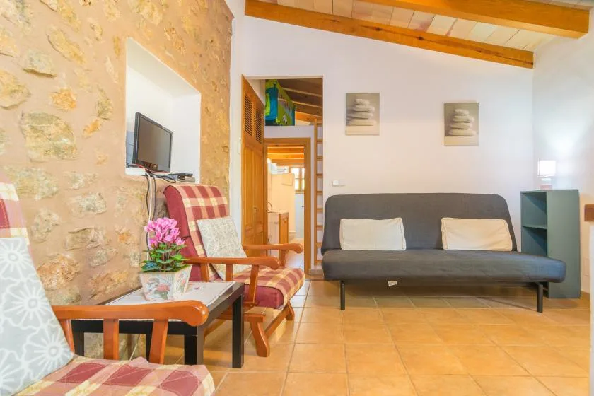 A living room with seating, a wall-mounted television, and exposed wooden ceiling beams.