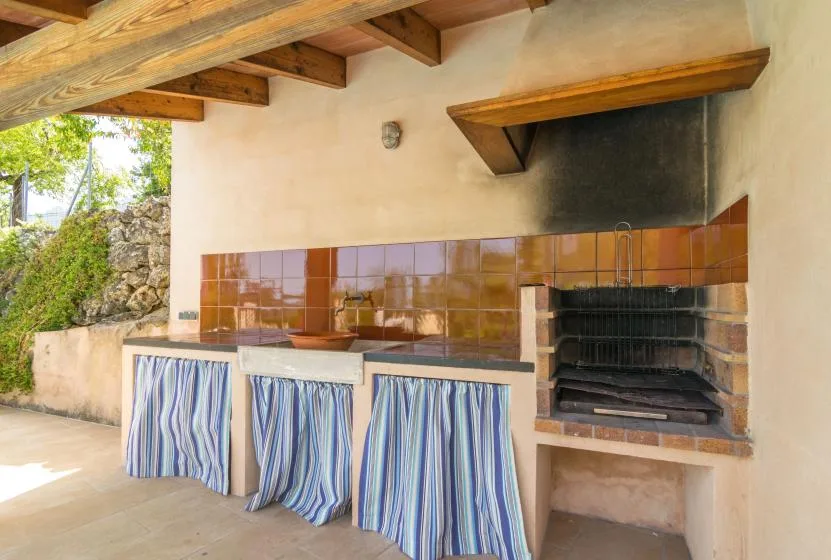 An outdoor cooking area with a tiled counter and built-in grill beneath a timber roof.
