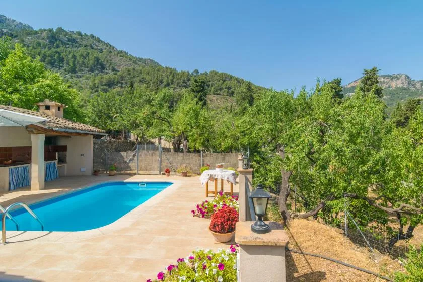 An outdoor swimming pool beside a patio, with green hills in the background.