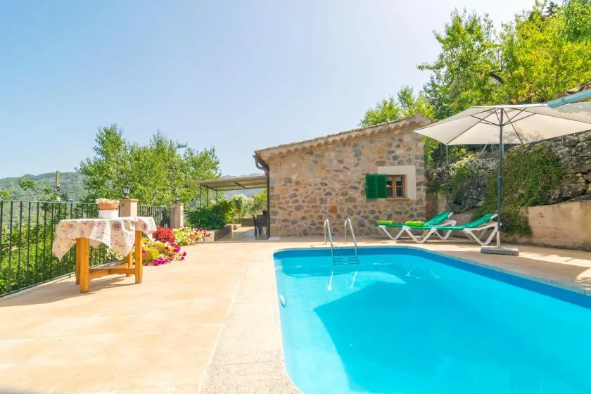 An outdoor swimming pool beside a stone building, with loungers and a patio umbrella.