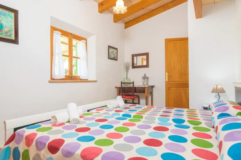A bedroom with colorful polka-dot bedding, a window, and exposed wooden ceiling beams.
