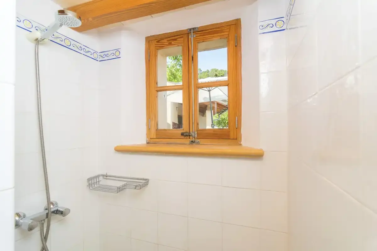 A tiled bathroom with a shower and a wooden-framed window.