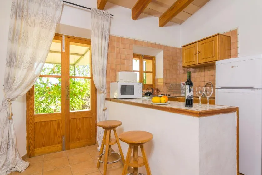 A compact kitchen with a breakfast counter, wooden stools, and a glass-paneled door.