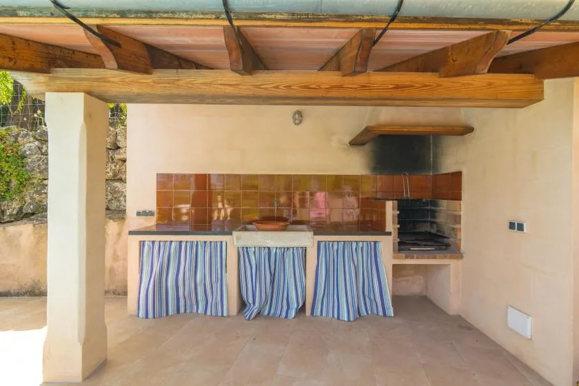 A covered outdoor kitchen with a counter, tiled backsplash, and built-in grill.